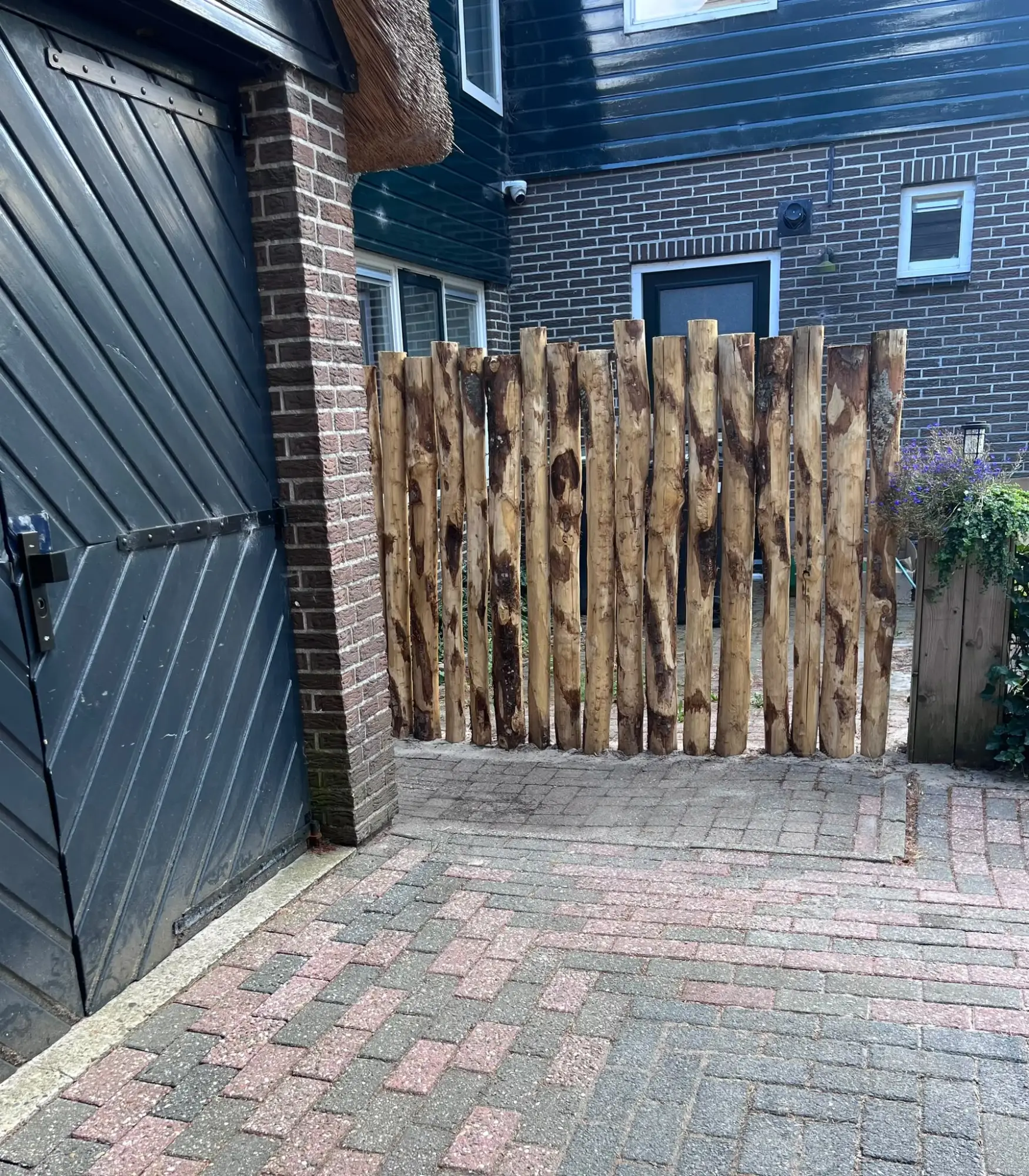 Hek van verticale rondhouten palen tussen woning en schuur