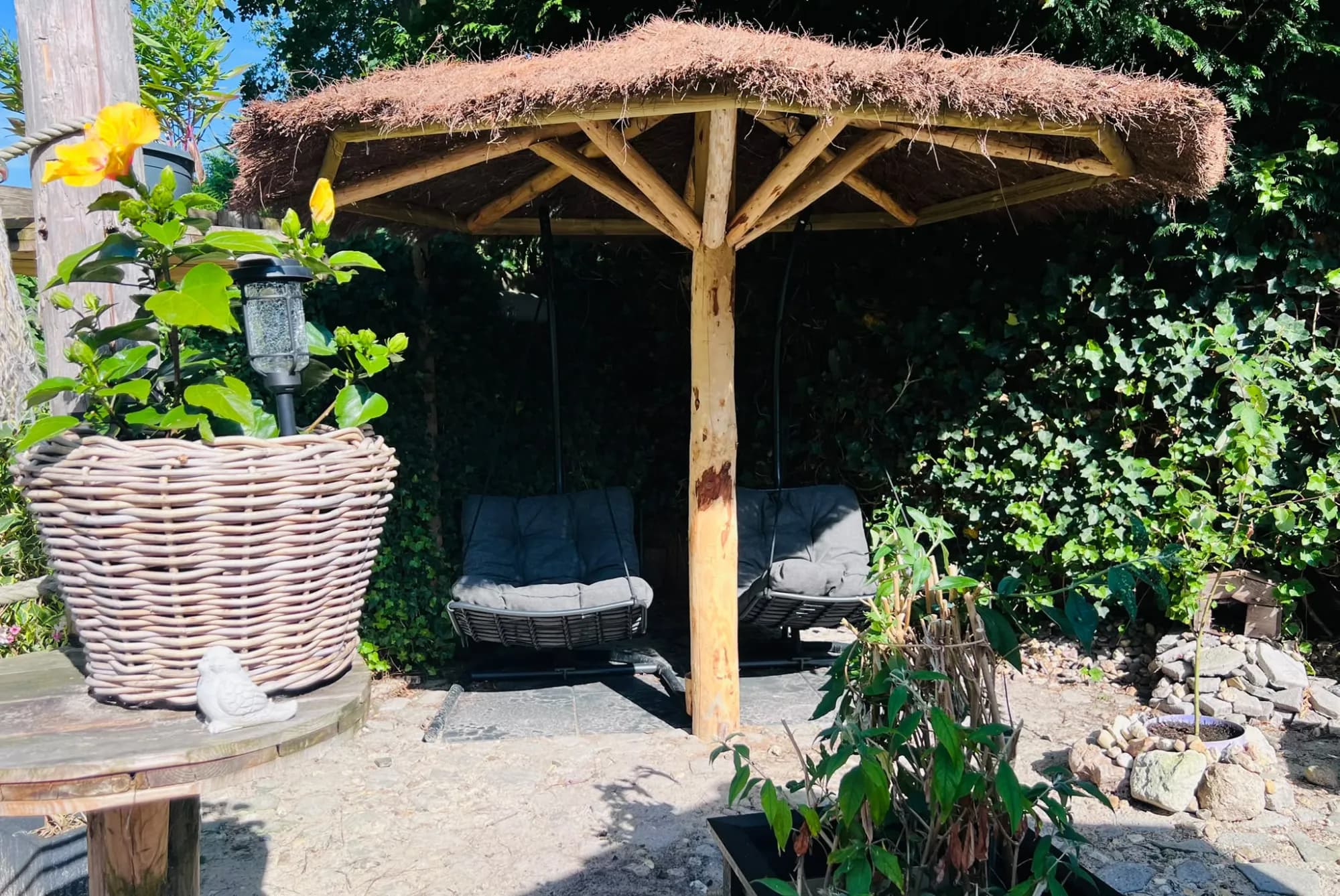 Houten parasol met rieten dak boven twee schommelstoelen